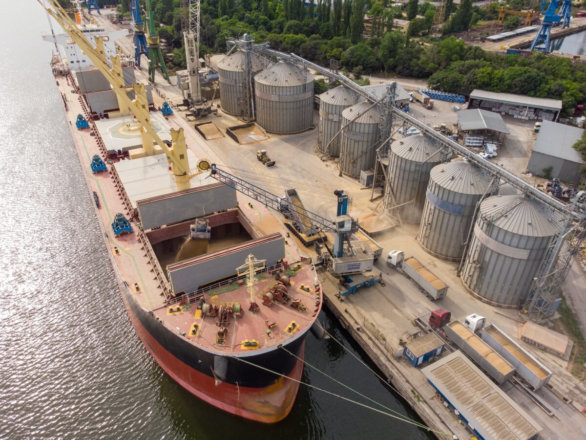 Loading grain into sea cargo vessel in seaport from silos of grain storage. Aerial view